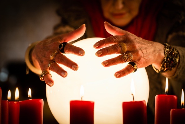 Woman in the background with a glowing crystal ball in the forefront.
